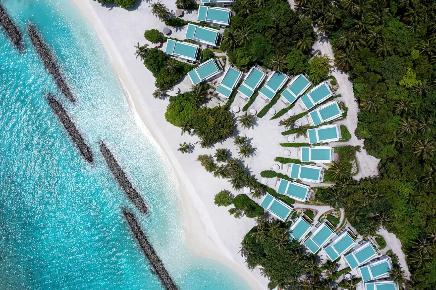 Aerial view of Niva Dhigali's fan-shaped run of villas curving along the beach, jungle behind and reef offshore