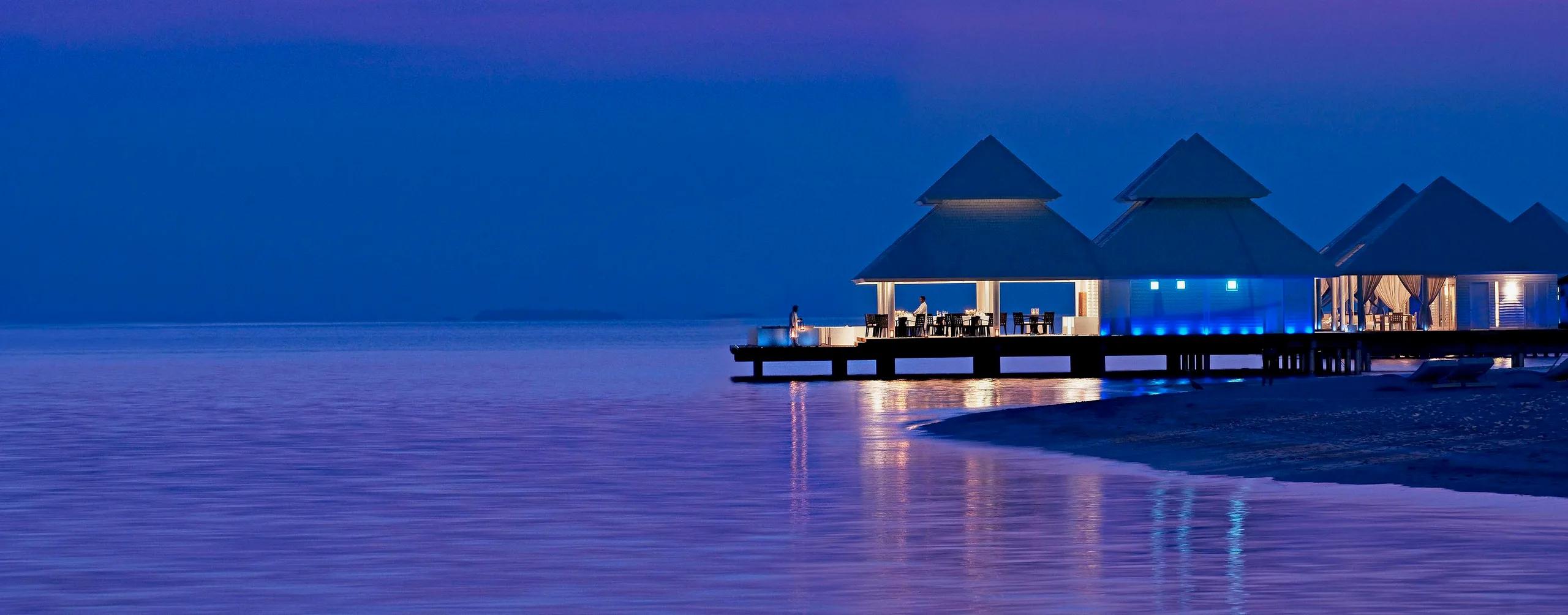 Thari Over Water Restaurant lit up at dusk, set on the jetty at Diamonds Athuruga