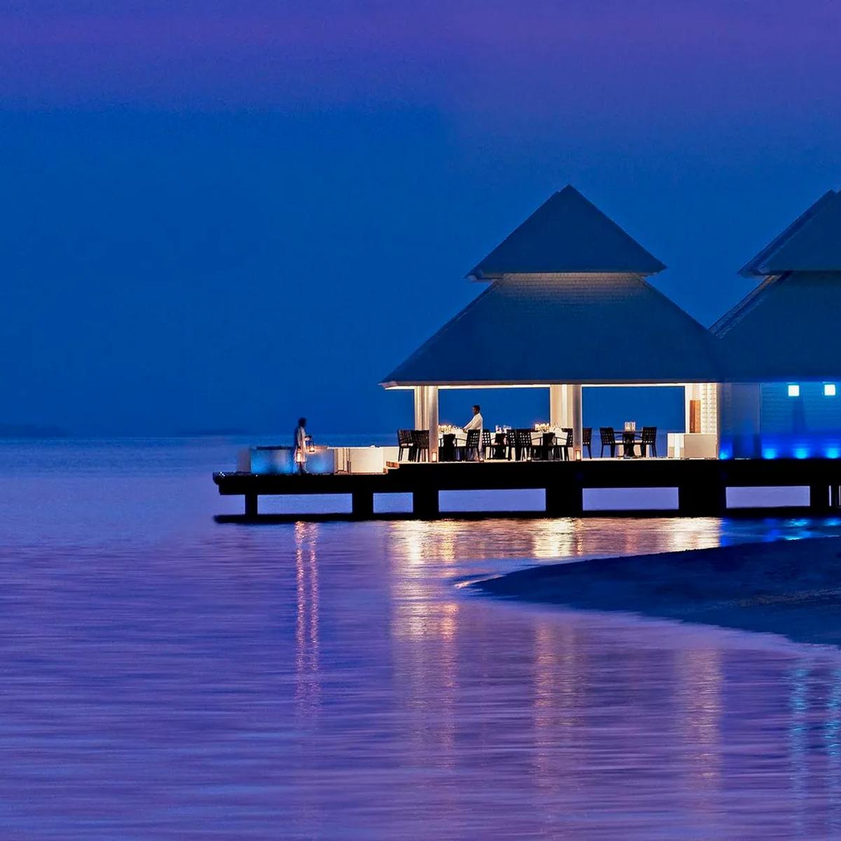 Thari Over Water Restaurant lit up at dusk, set on the jetty at Diamonds Athuruga