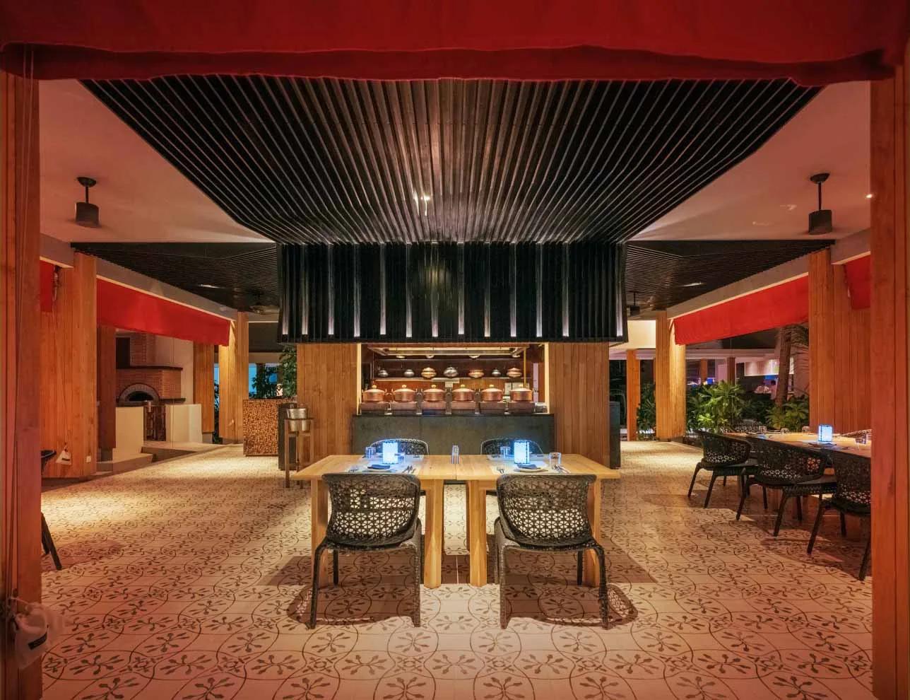 EAST's dining room at Amilla in the evening, red drapery over an open kitchen lined with copper cookware