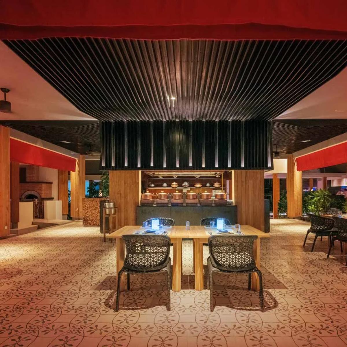 EAST's dining room at Amilla in the evening, red drapery over an open kitchen lined with copper cookware