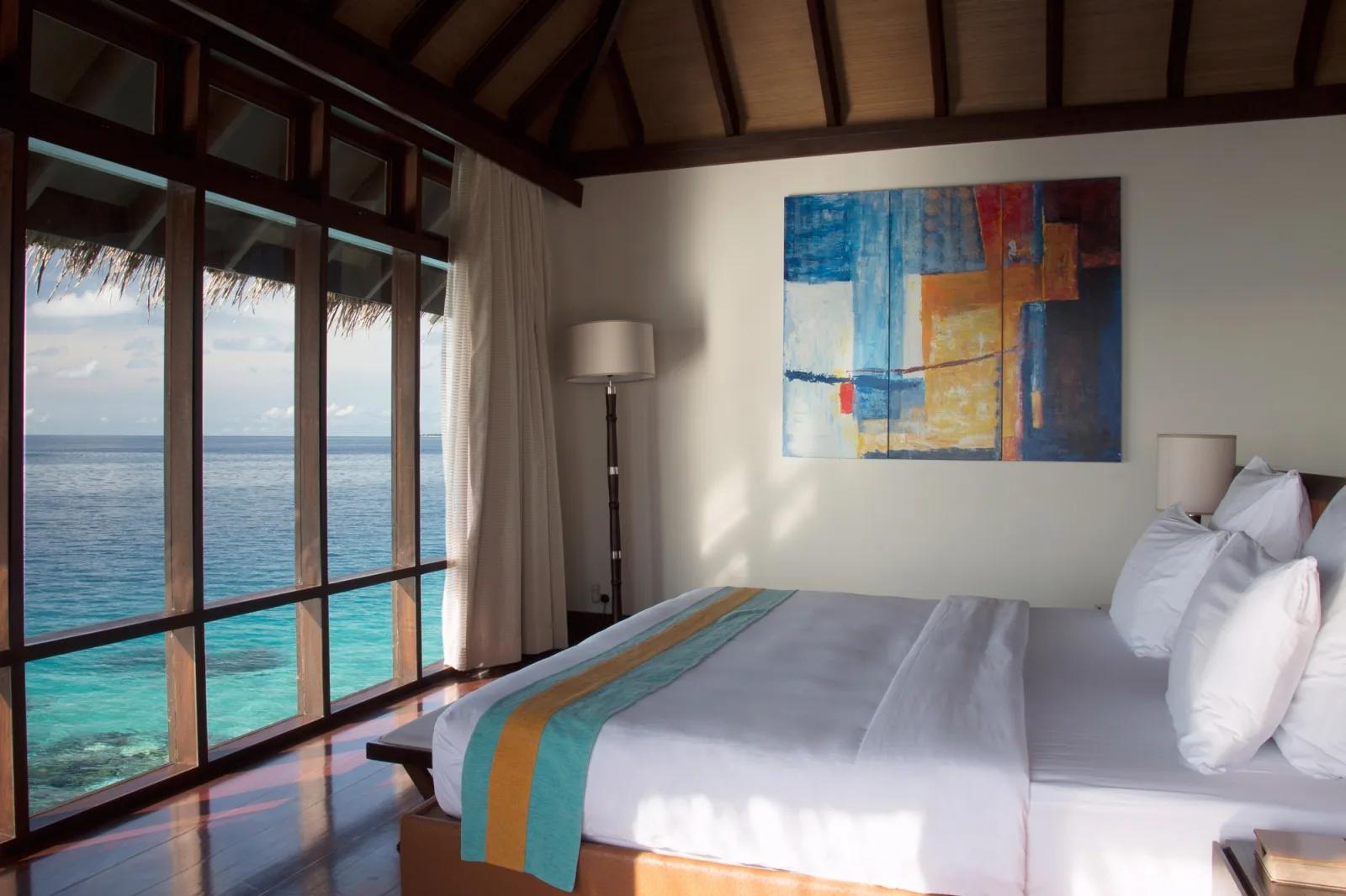 Bedroom of an Escape Water Villa with Pool, abstract painting on the wall and glass doors opening onto the lagoon