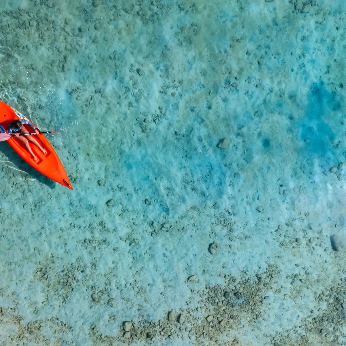 A single kayak crossing NH Maldives Kuda Rah's shallow, clear lagoon, seen from above