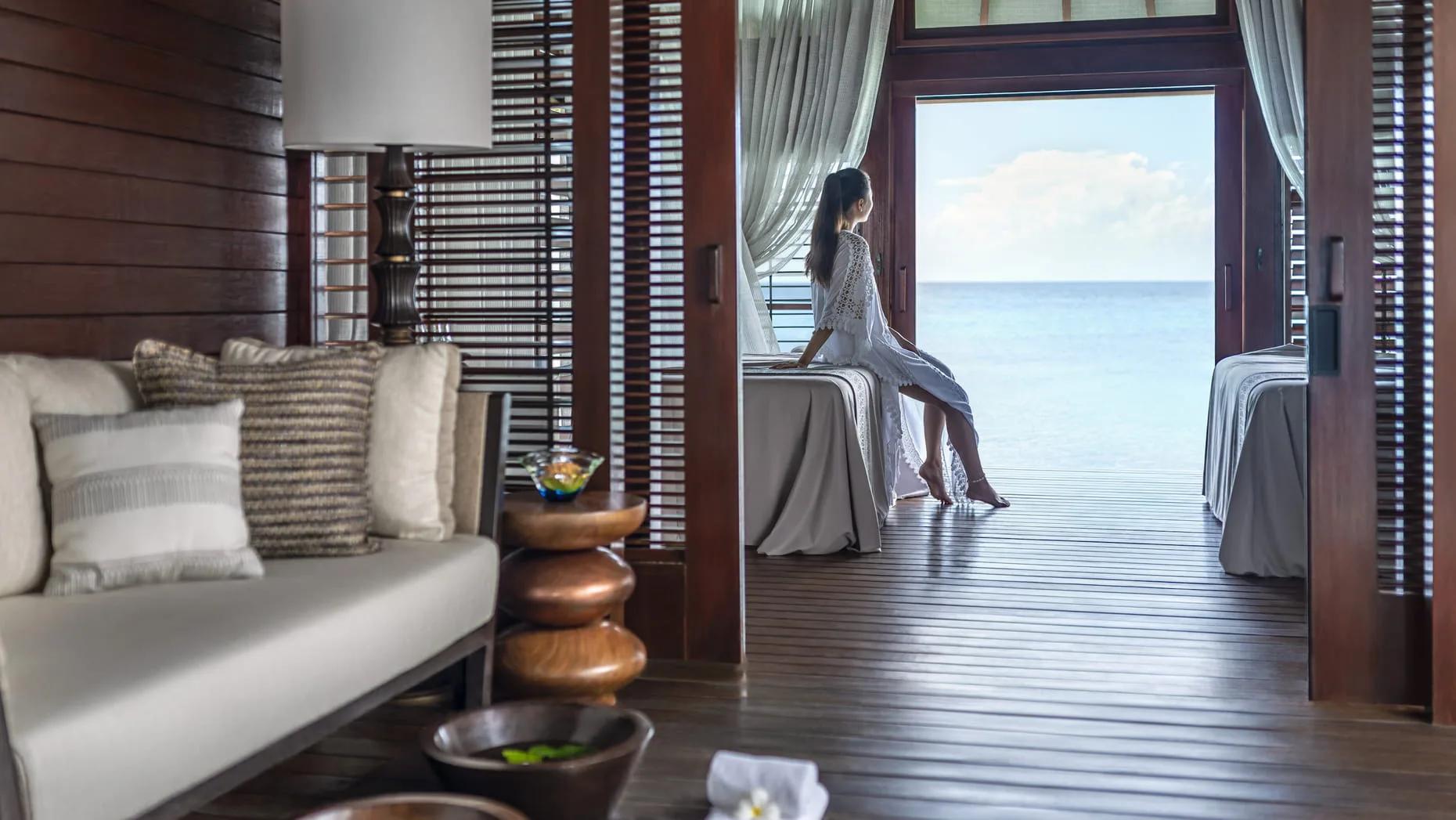 A guest seated in an overwater treatment pavilion at ŪRJĀ spa, the ocean visible through the open doors