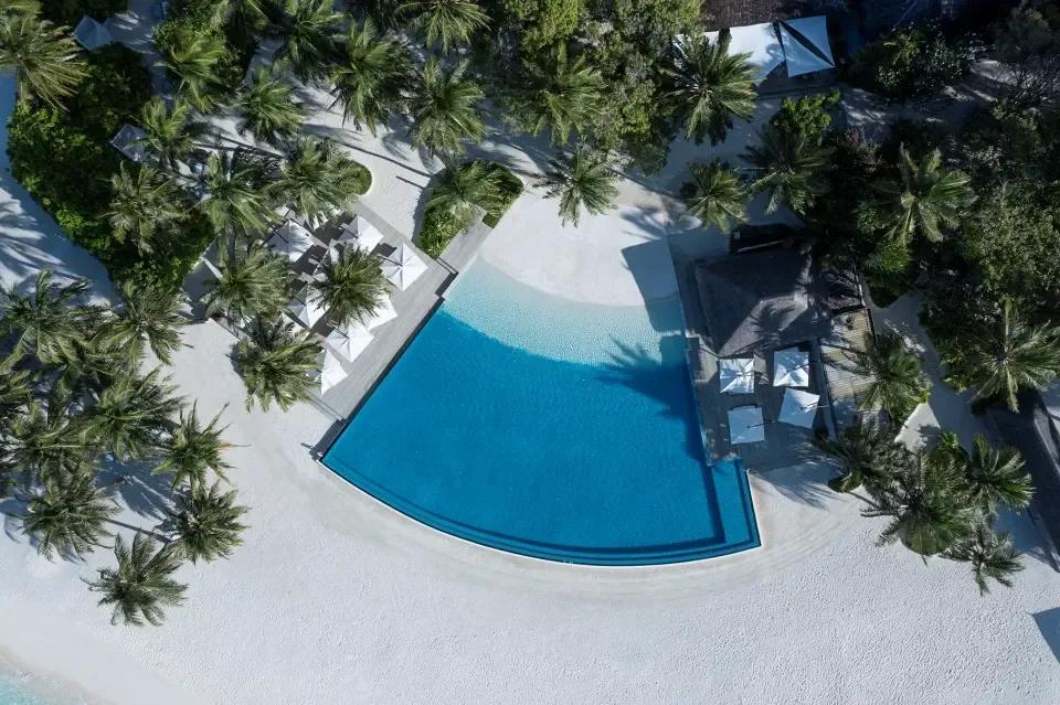 A top-down view of Velassaru's freeform infinity pool, ringed by loungers and palms