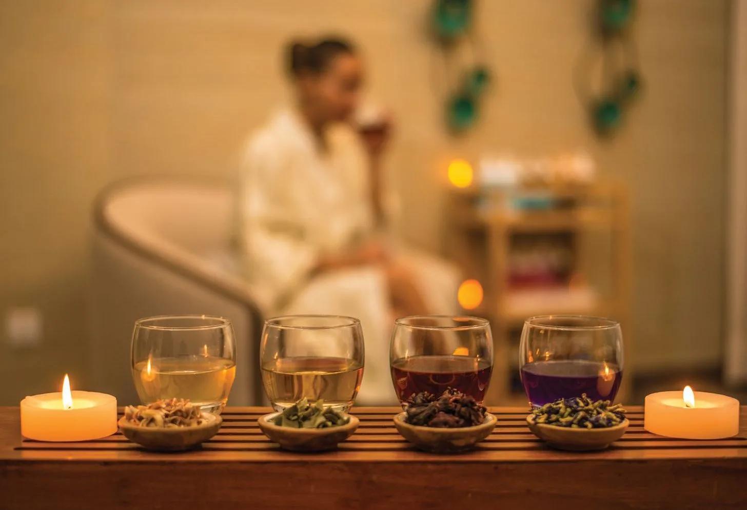 A guest in a robe sampling a flight of herbal teas by candlelight after a spa treatment