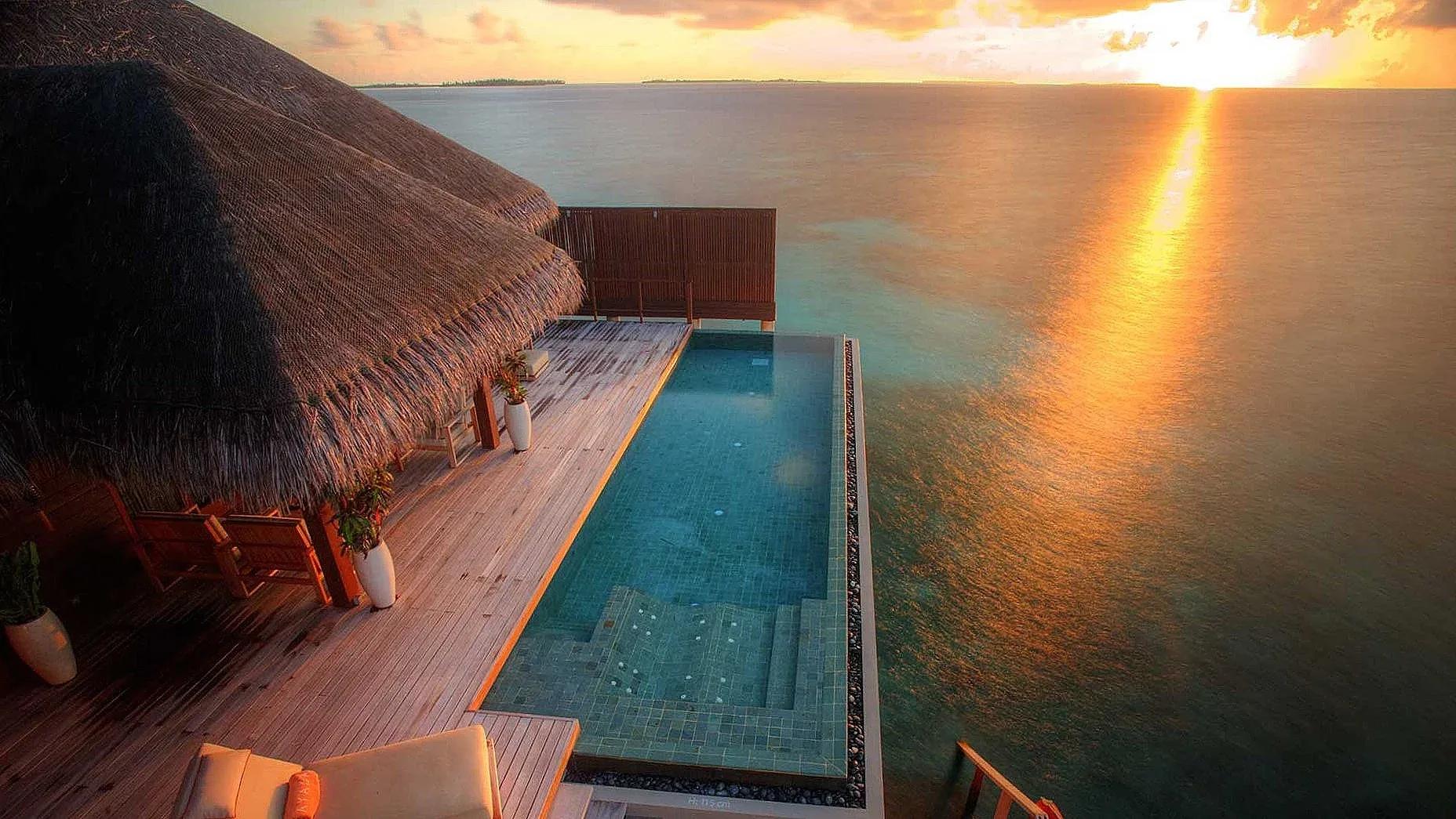 A private plunge pool cantilevered off an overwater villa deck at sunset, open ocean and a distant island beyond