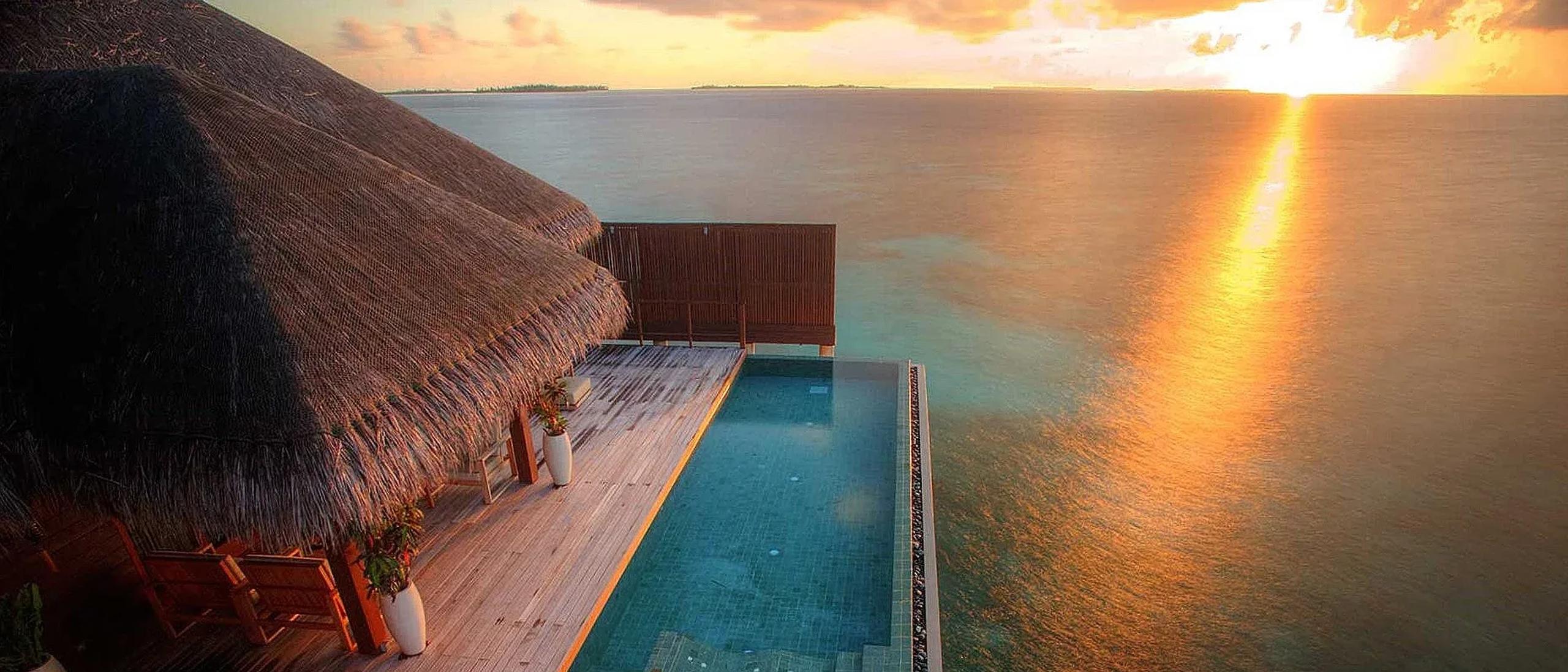 A private plunge pool cantilevered off an overwater villa deck at sunset, open ocean and a distant island beyond