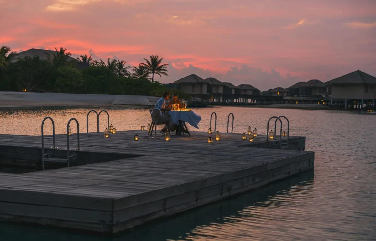 A private table set for two on an overwater pontoon at dusk, part of the resort's bespoke dining programme