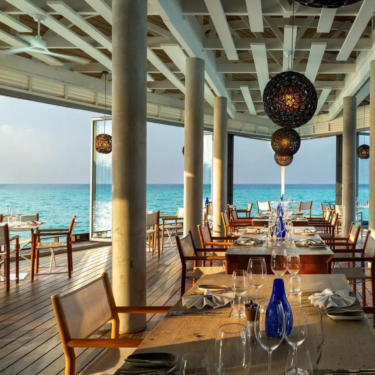 The Reef, Kuramathi's waterfront restaurant, set tables facing the open lagoon with a row of overwater villas visible in the distance at dusk