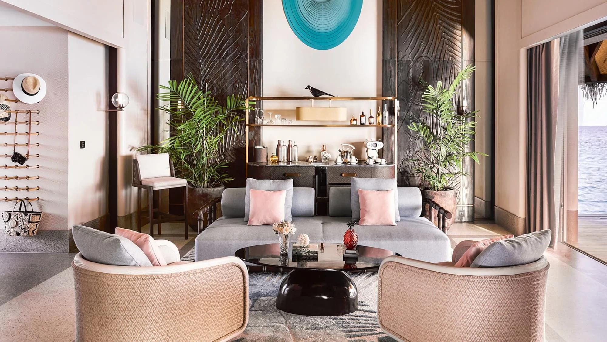 The living room of a Luxury Water Villa with Pool, with a bar cart, bookshelf and the lagoon visible through the doorway
