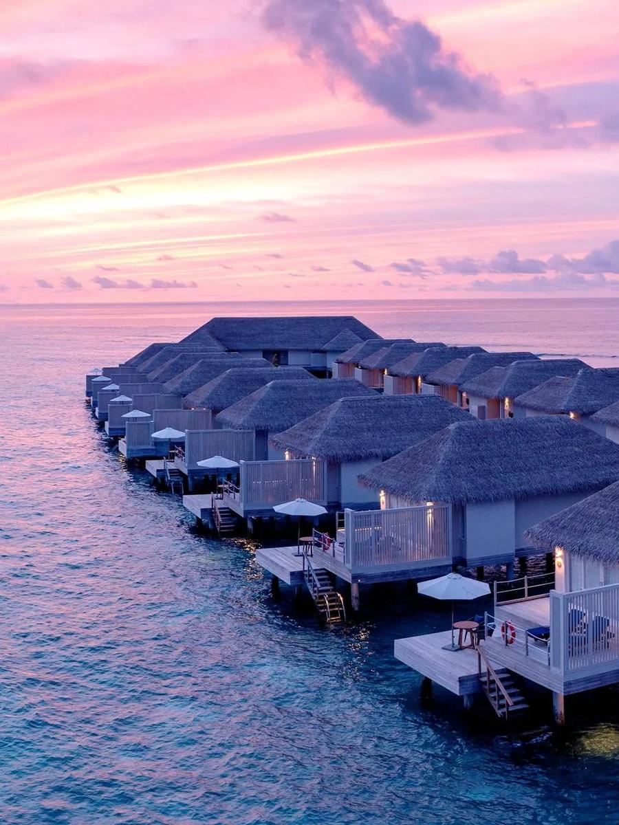 A row of overwater Sunset Water Villas at Baglioni Maldives under a pink and purple dusk sky
