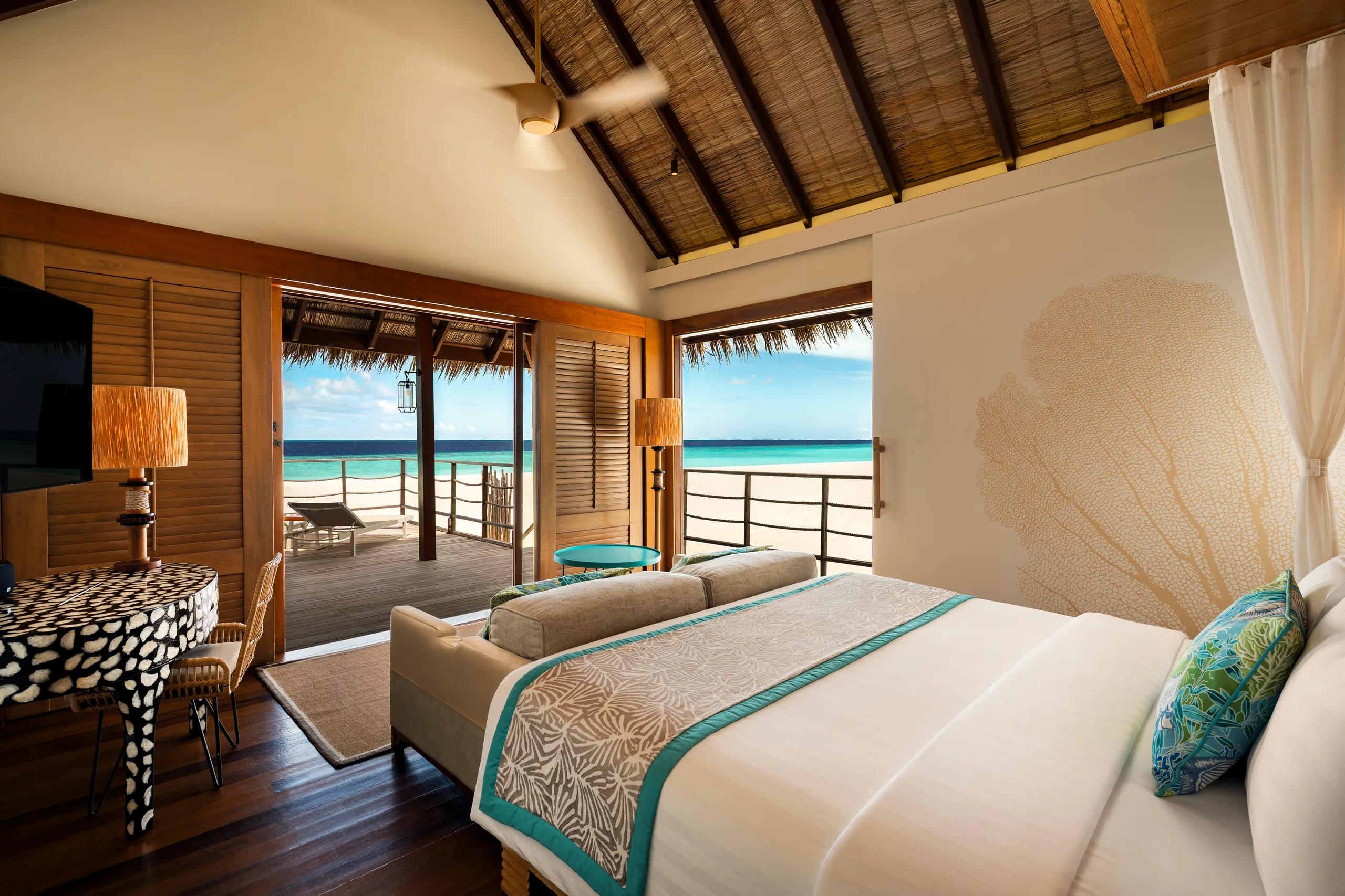 Senior Sand Villa bedroom with a wood-panelled headboard, pendant lighting, and a door opening onto a sandy garden path