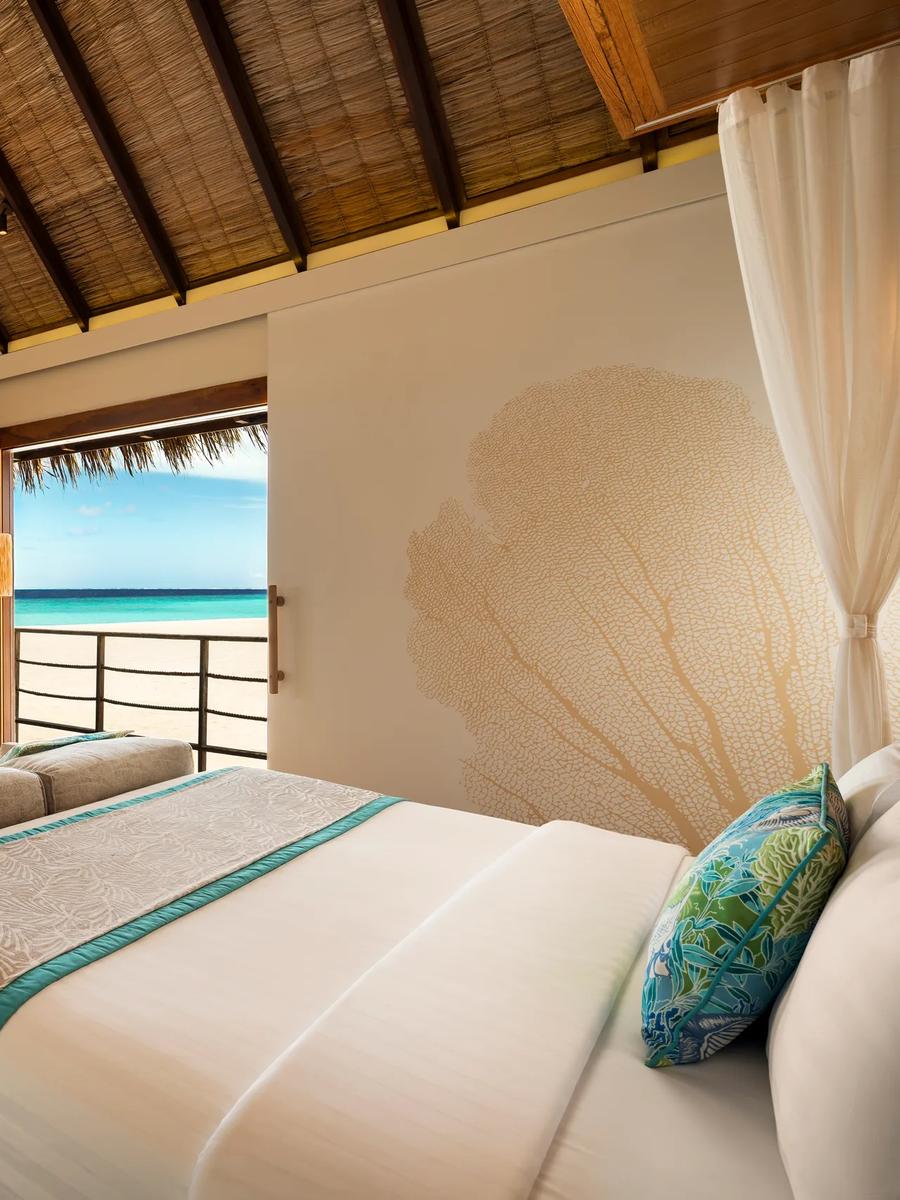 Senior Sand Villa bedroom with a wood-panelled headboard, pendant lighting, and a door opening onto a sandy garden path