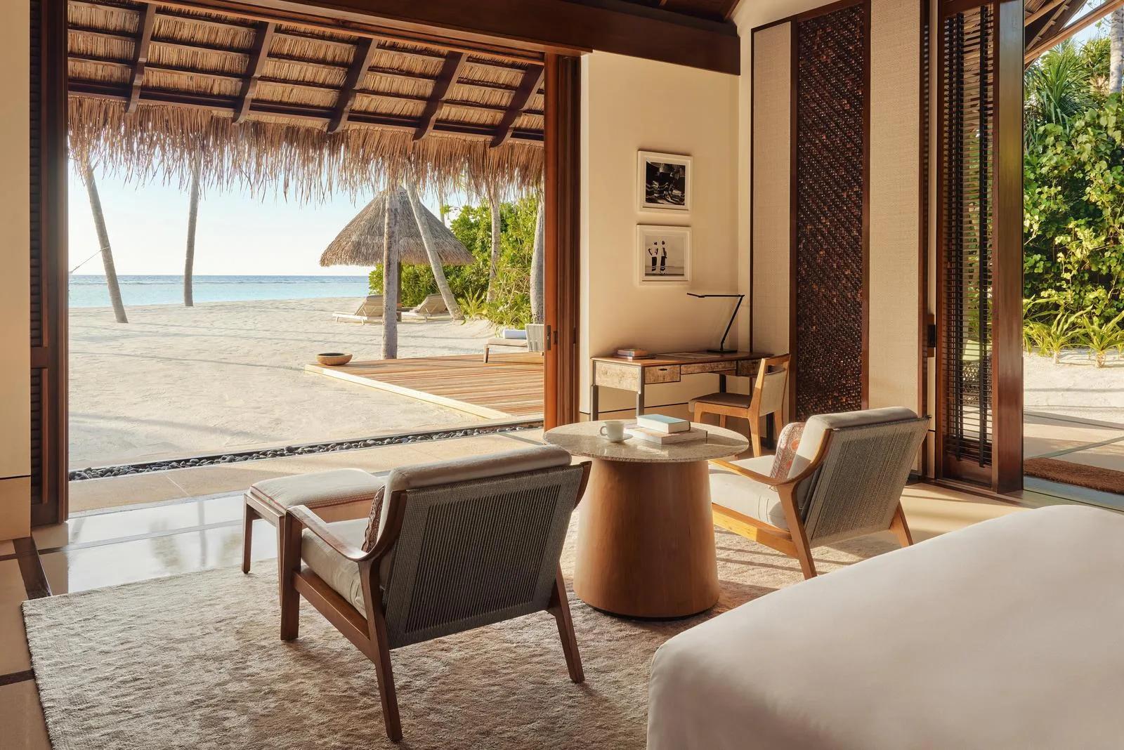 The bedroom of a Beach Villa at One&Only Reethi Rah, opening under a thatched veranda roof onto the beach and a private pool