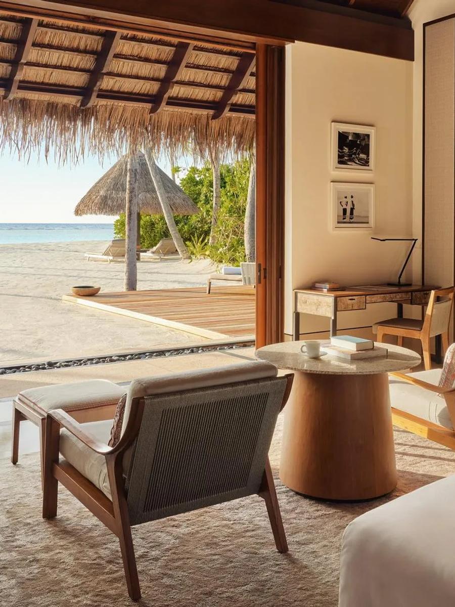 The bedroom of a Beach Villa at One&Only Reethi Rah, opening under a thatched veranda roof onto the beach and a private pool