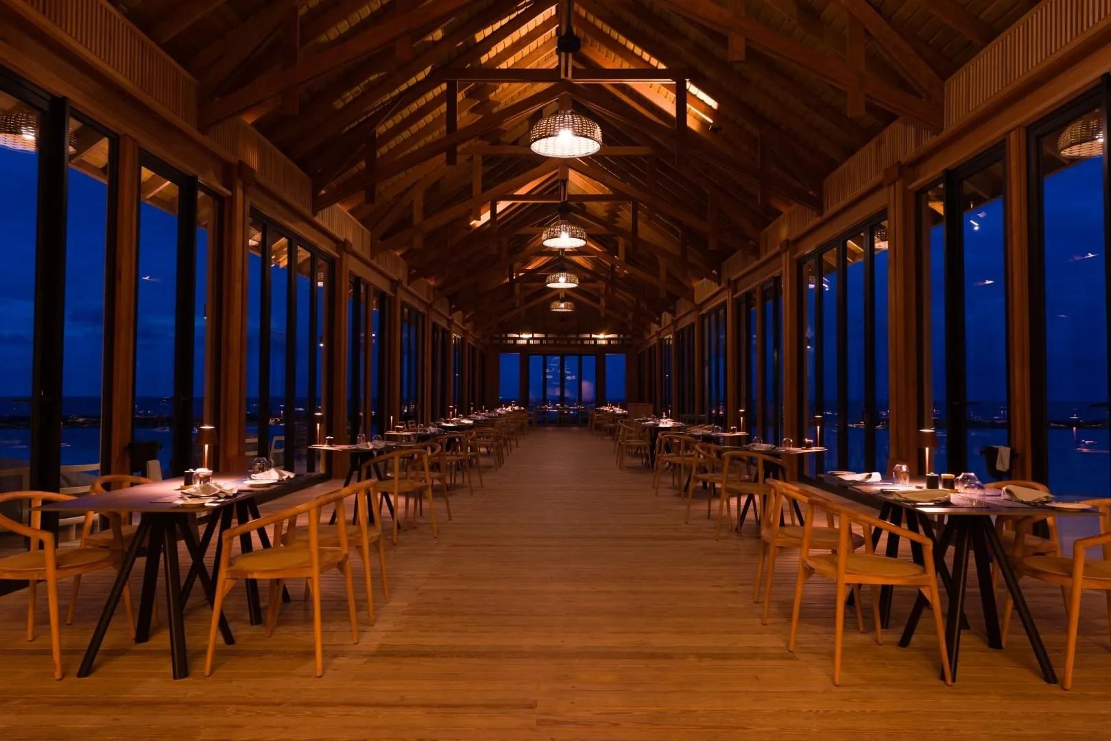 The Flame's open-sided timber dining hall in the evening, sea visible on both sides