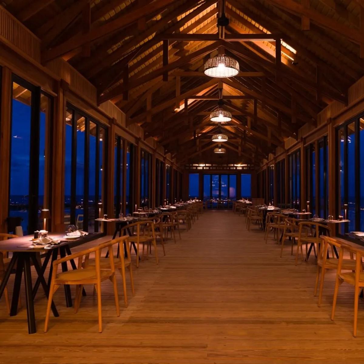 The Flame's open-sided timber dining hall in the evening, sea visible on both sides