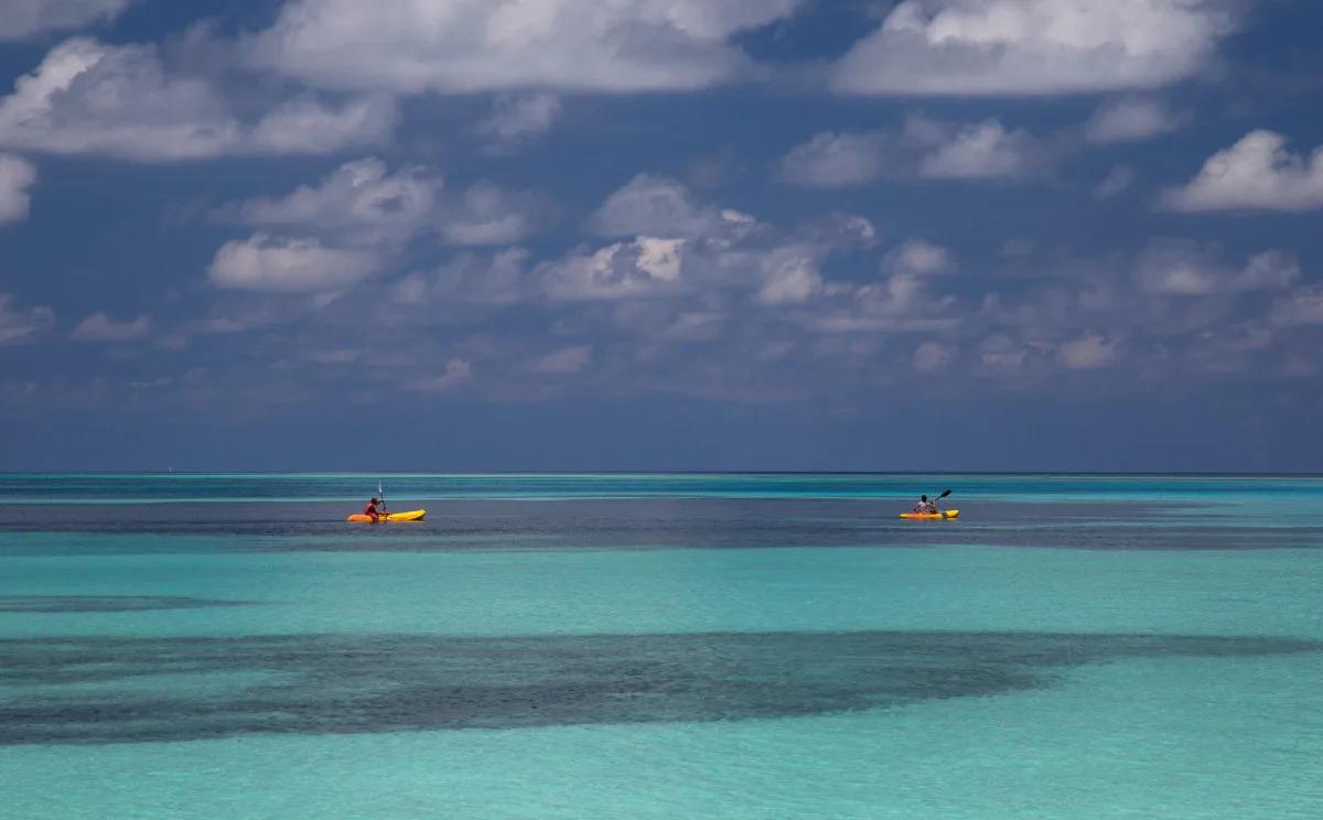 Two kayakers paddling across the lagoon, seen from a distance against a partly cloudy sky