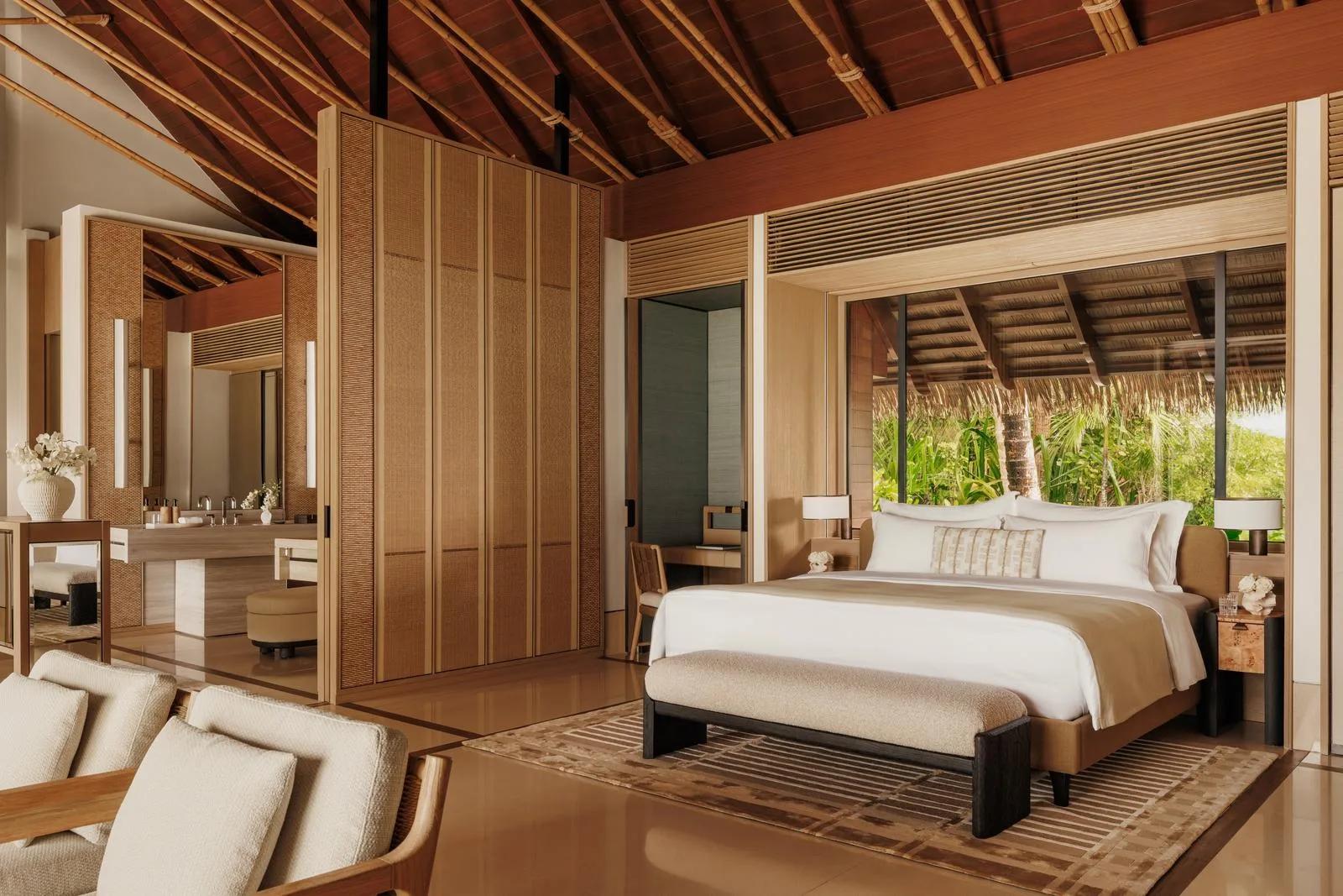 A bedroom at a Grand Residence, One&Only Reethi Rah, with glass doors opening onto dense island greenery