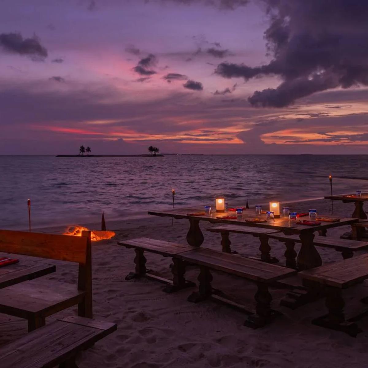 BBQ Shak's lantern-lit beach dinner tables at dusk, a small island silhouetted on the horizon