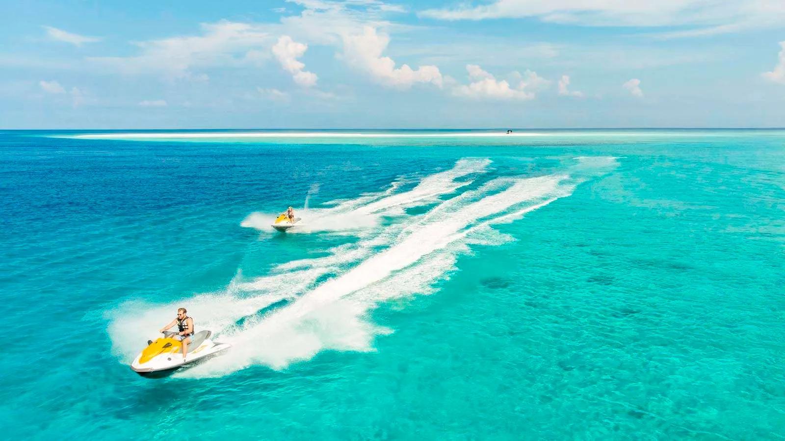 Two jet skis cutting wakes across the lagoon towards a distant sandbank