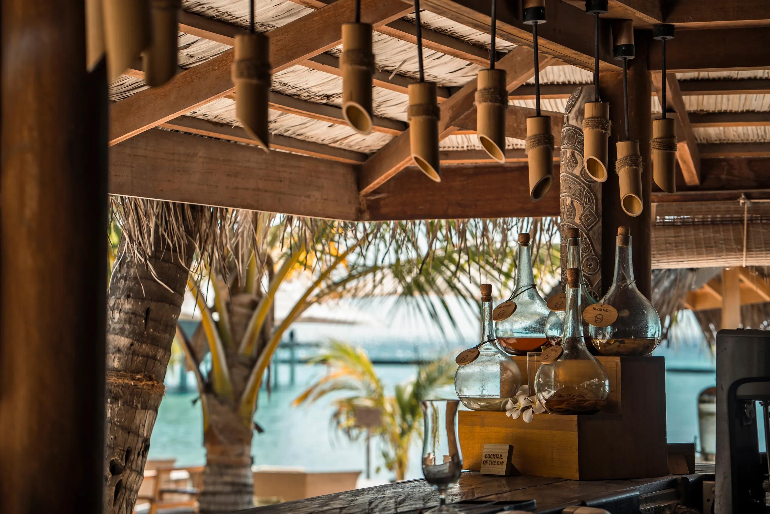 Close view of Totem Bar's counter, glass spirit decanters catching the evening light, the pool visible beyond