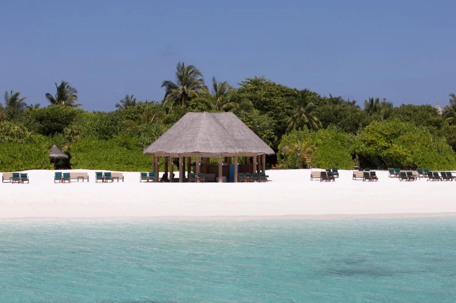 A thatched beachfront pavilion with loungers either side, seen from the water