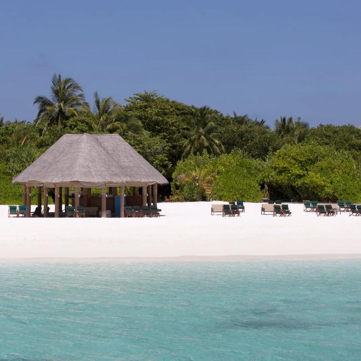 A thatched beachfront pavilion with loungers either side, seen from the water
