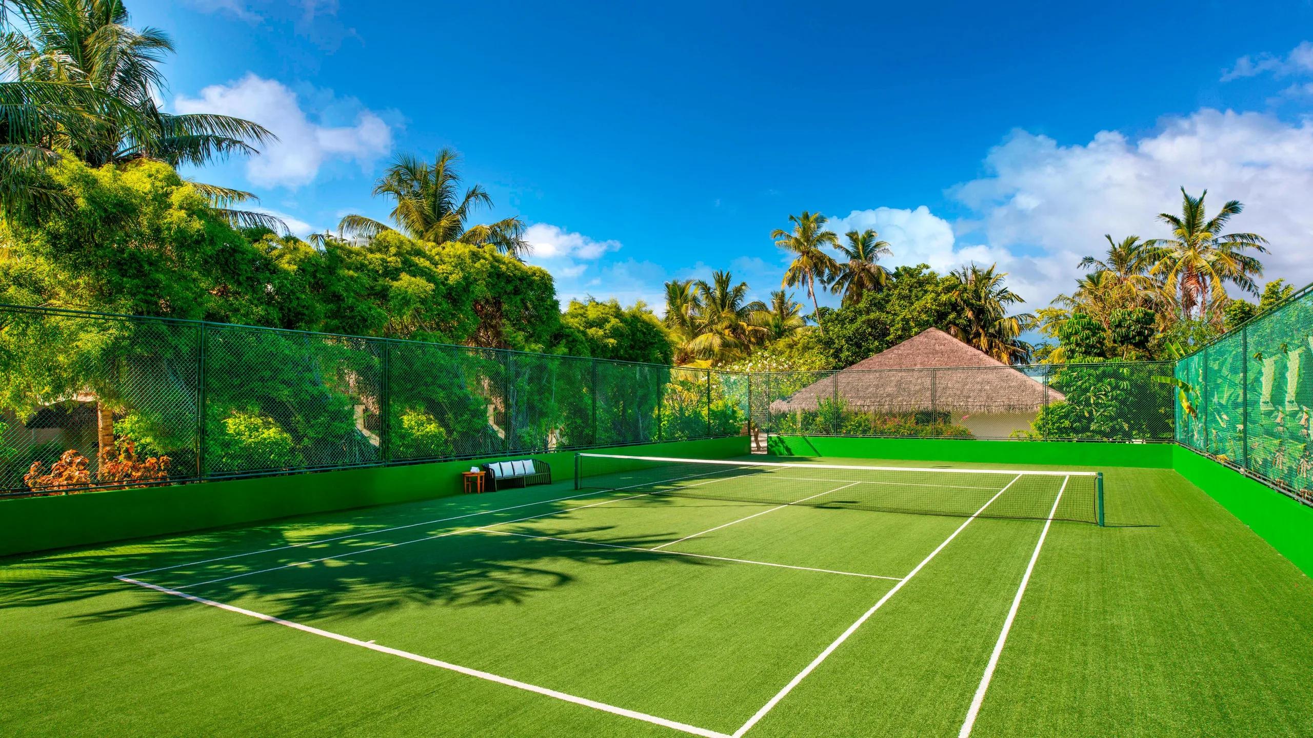 The resort's tennis court, enclosed by green fencing and framed by palm trees