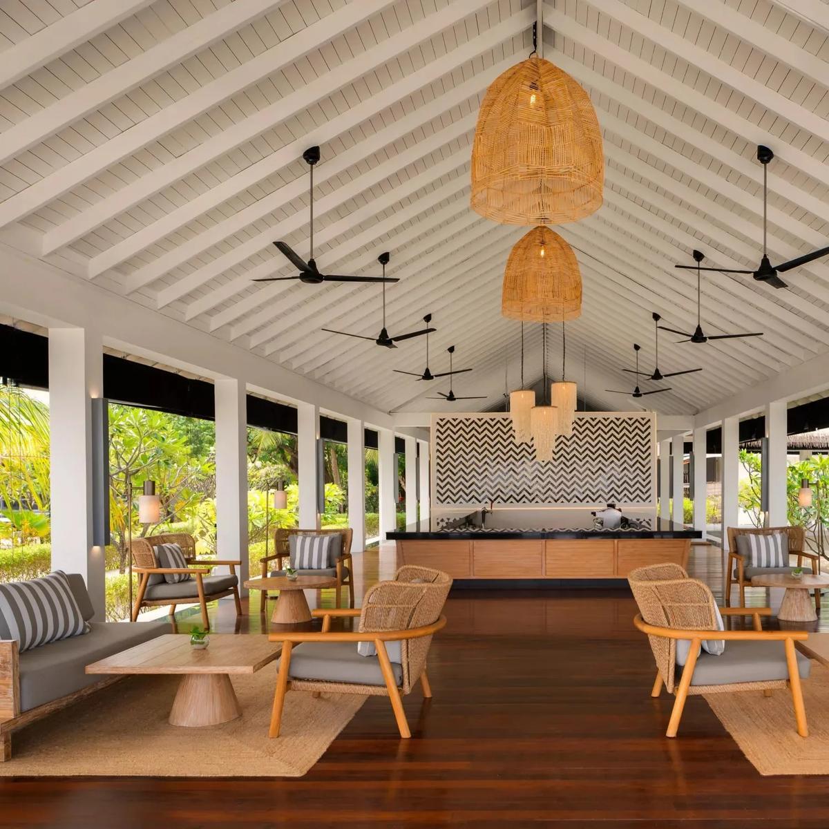 An open-air lounge and bar area at Noku Maldives, rattan seating beneath a vaulted thatched ceiling