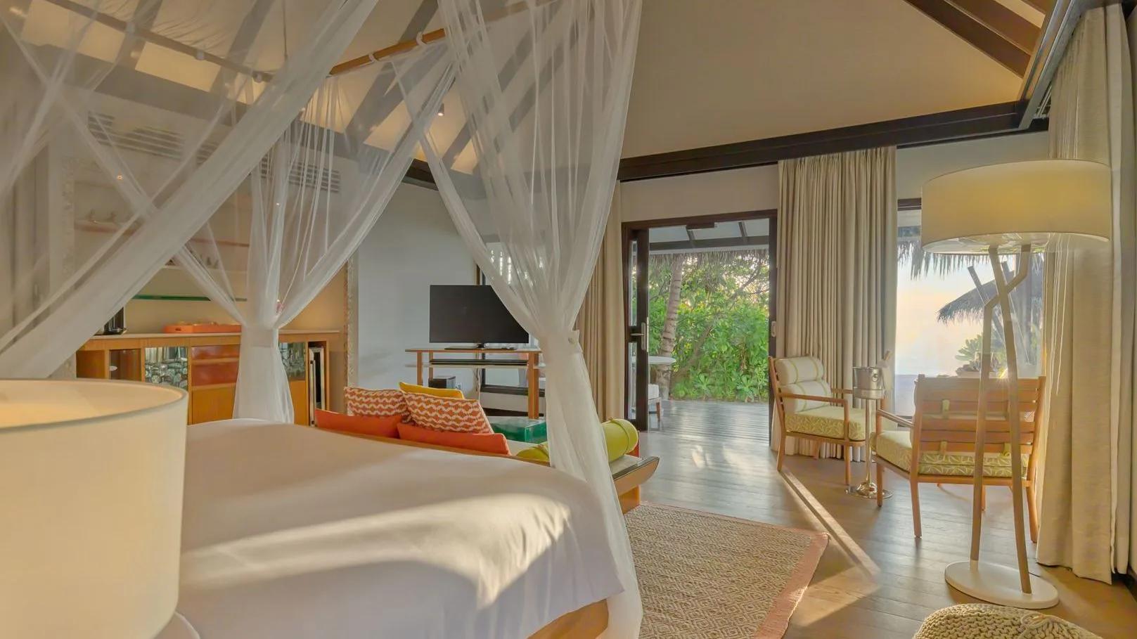 A canopied villa bed with doors folded back to the villa's wooden deck