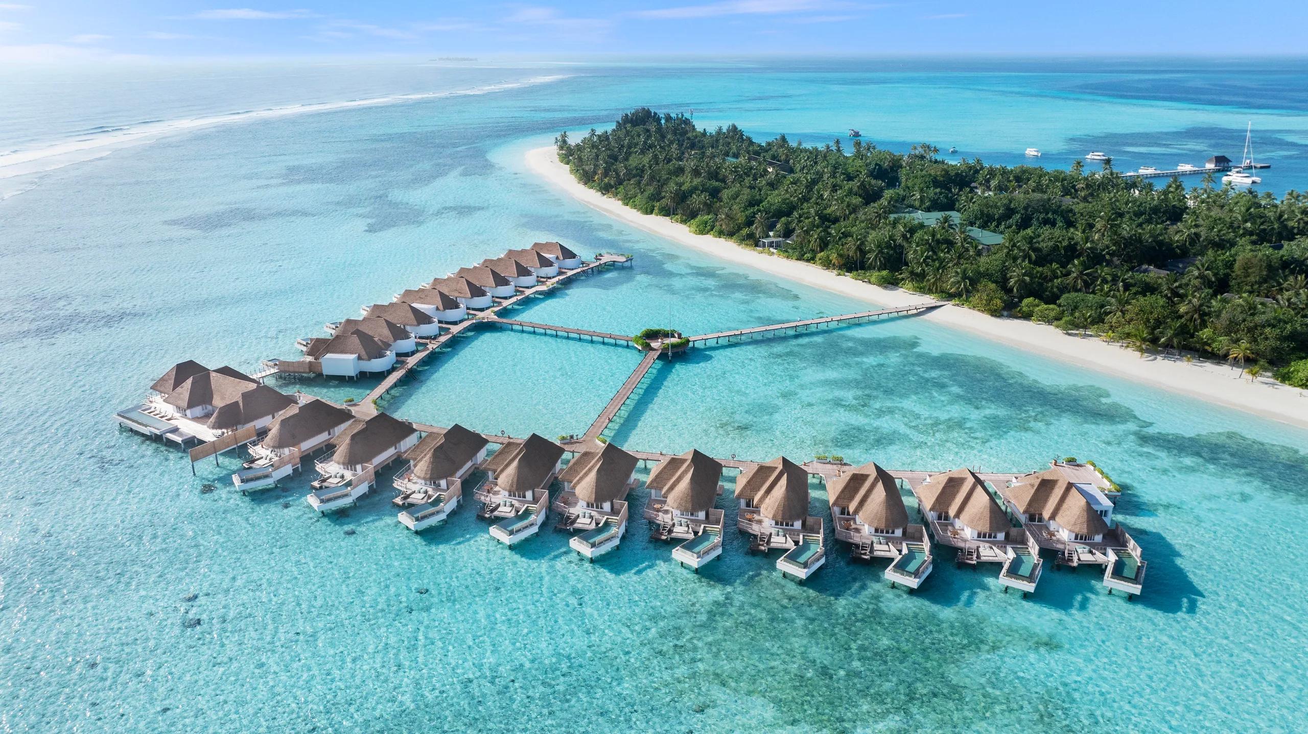 Aerial view of Six Senses Kanuhura's overwater villas arranged in a V-shaped jetty over the turquoise lagoon.