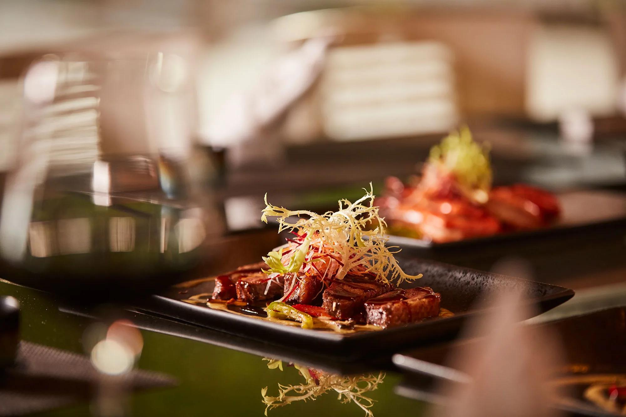 A finely plated dish with fresh herbs and chilli on a dark plate, representative of Iru Fushi's casual dining counters — dedicated La Cremeria photography to follow