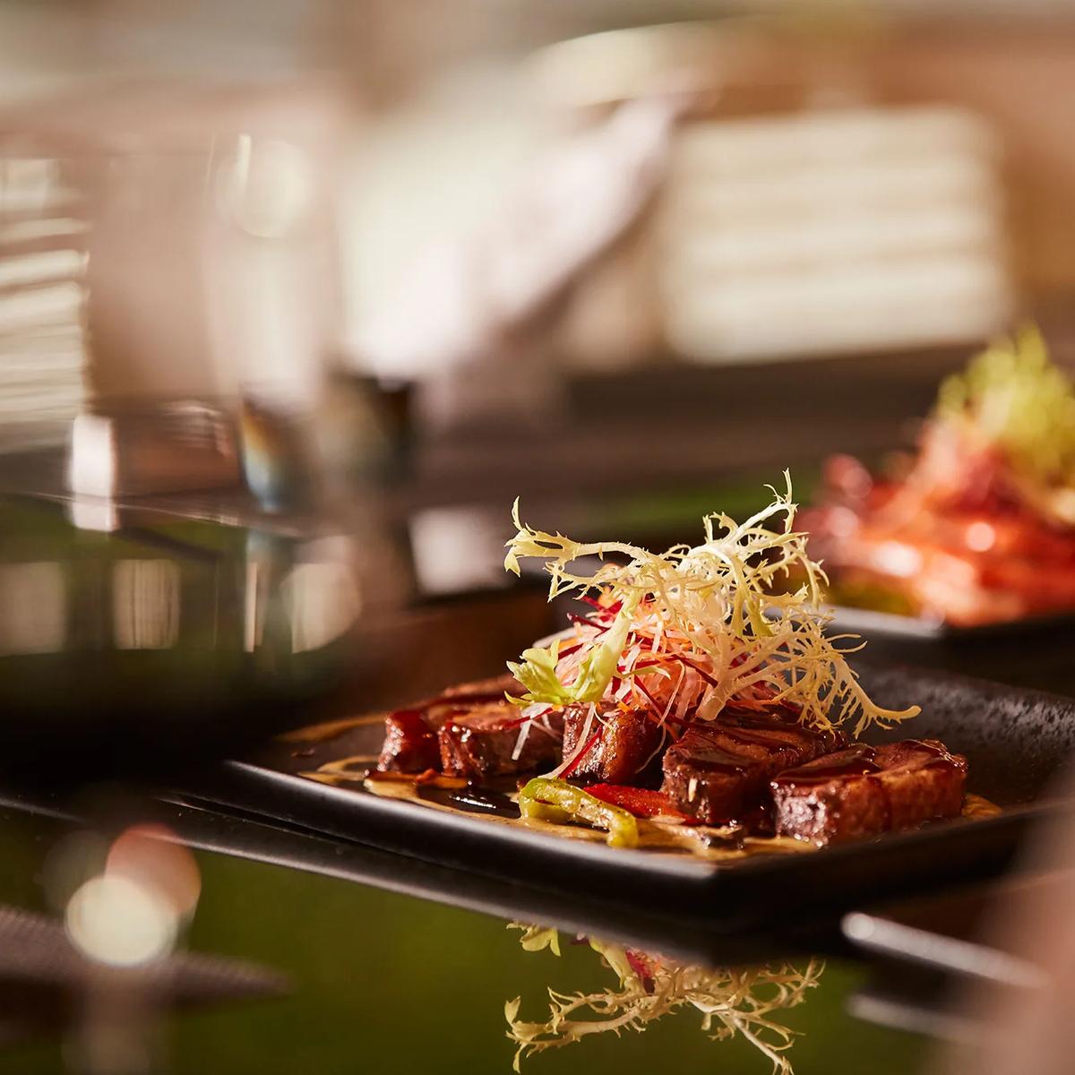 A finely plated dish with fresh herbs and chilli on a dark plate, representative of Iru Fushi's casual dining counters — dedicated La Cremeria photography to follow