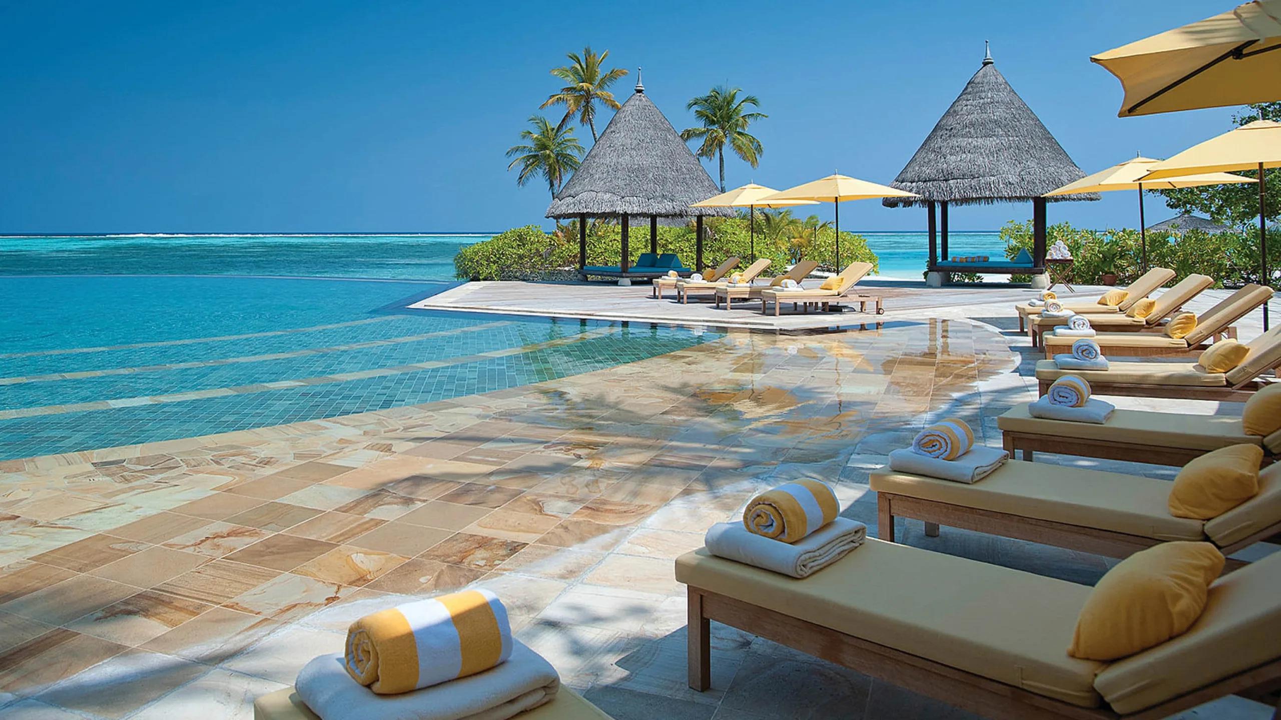 The main infinity pool with loungers and thatched cabanas facing the lagoon
