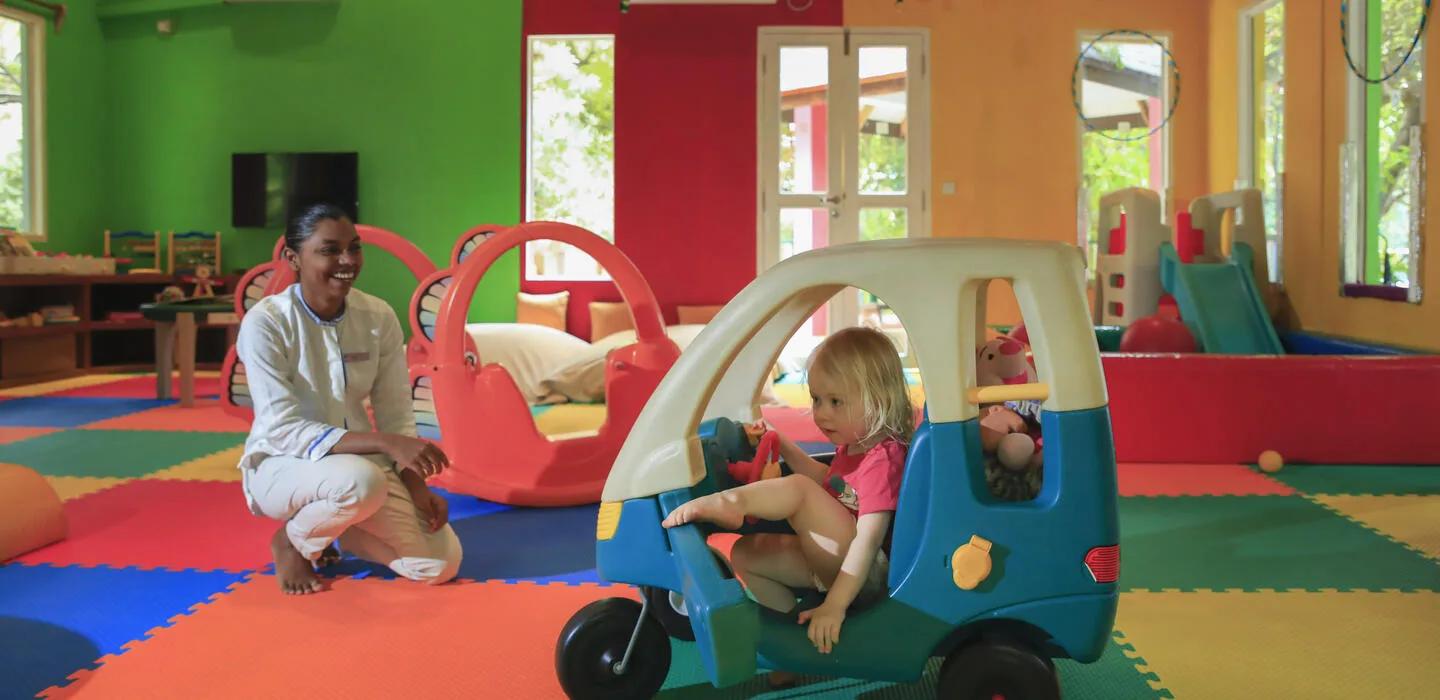 A Camp Safari staff member kneeling beside a young guest playing in the kids' club