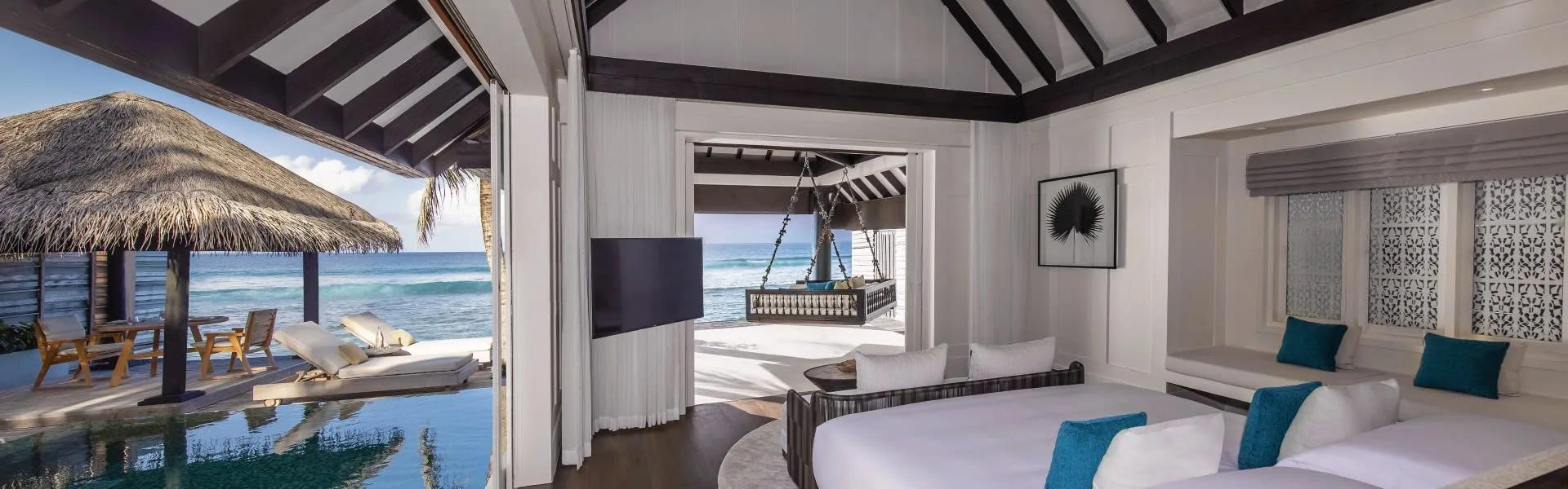 Inside an Ocean House with Pool, the bedroom opening onto a thatched poolside pavilion and the ocean beyond, with a swing daybed on the adjoining deck