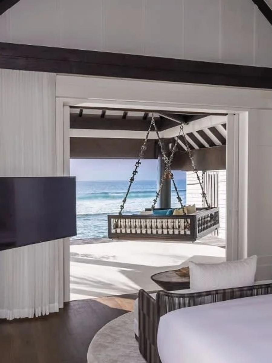 Inside an Ocean House with Pool, the bedroom opening onto a thatched poolside pavilion and the ocean beyond, with a swing daybed on the adjoining deck