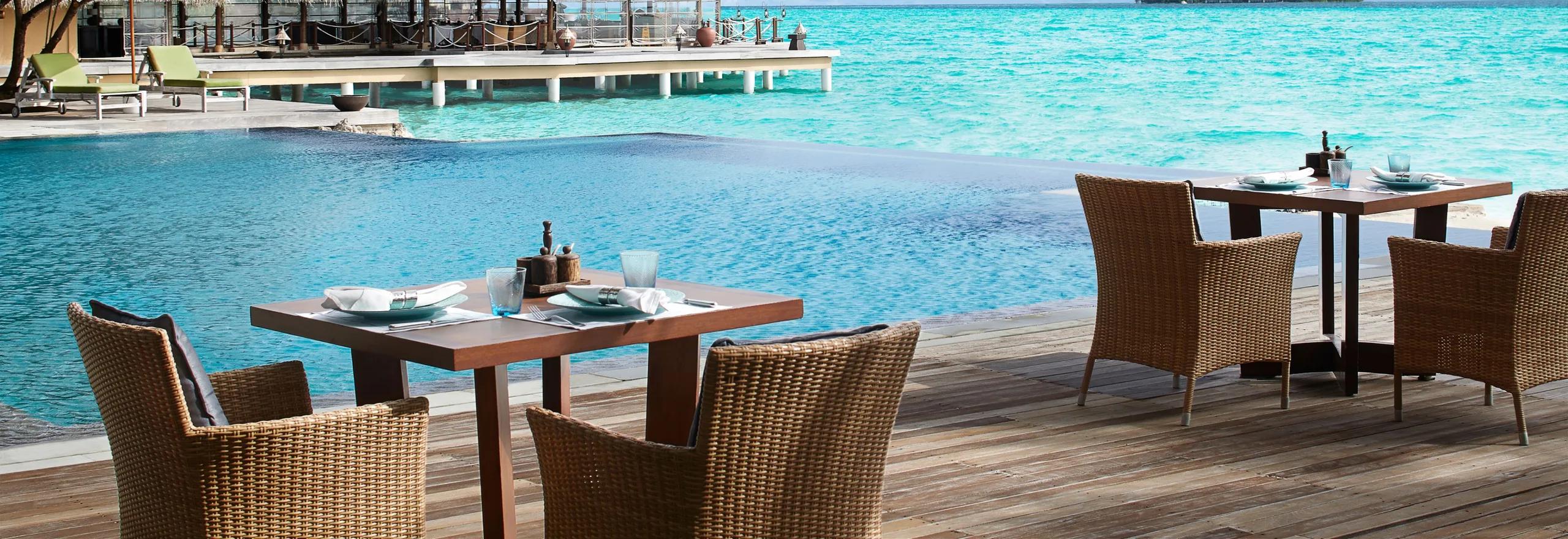 Mediterraneo Waterfront's poolside deck, tables set beside the infinity-edge pool with the lagoon and a distant island beyond