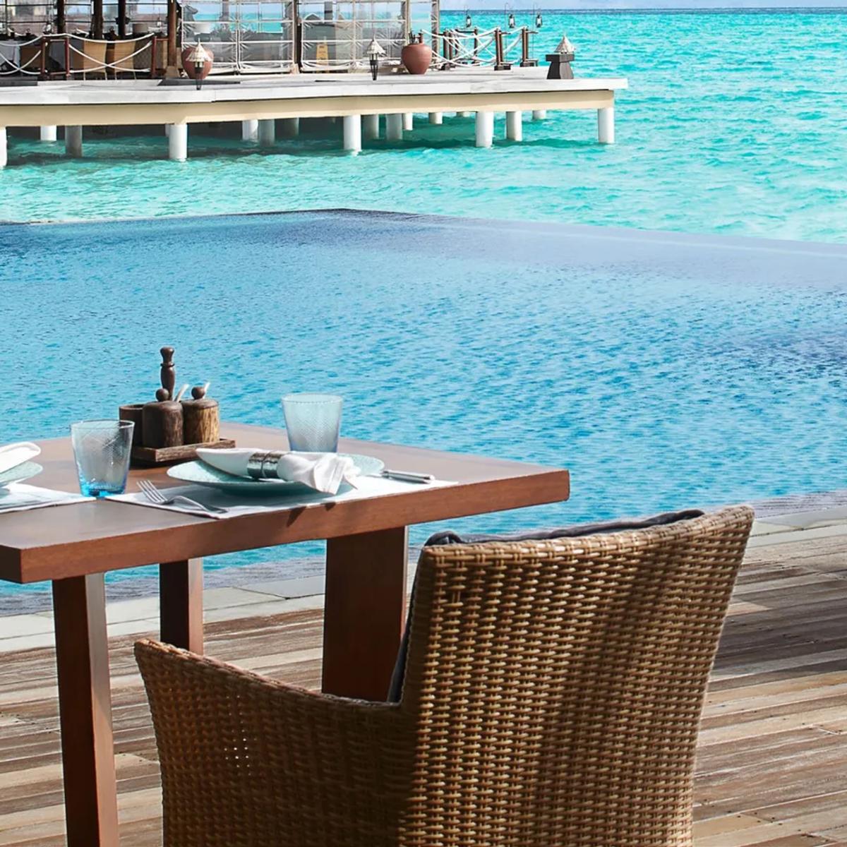 Mediterraneo Waterfront's poolside deck, tables set beside the infinity-edge pool with the lagoon and a distant island beyond