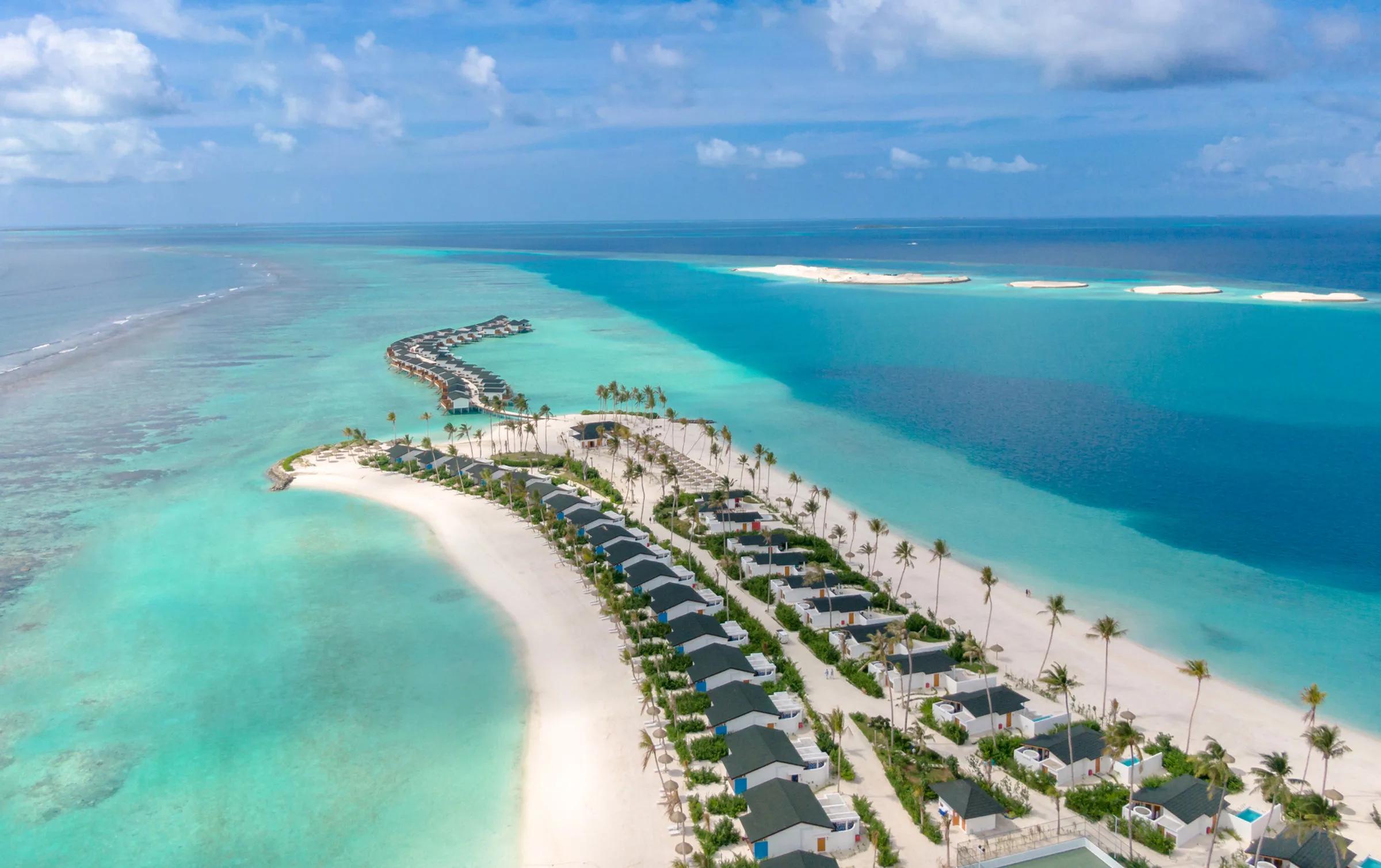 An aerial view of Joy Island's butterfly-shaped outline, overwater villas snaking into the lagoon beside a row of beachfront villas