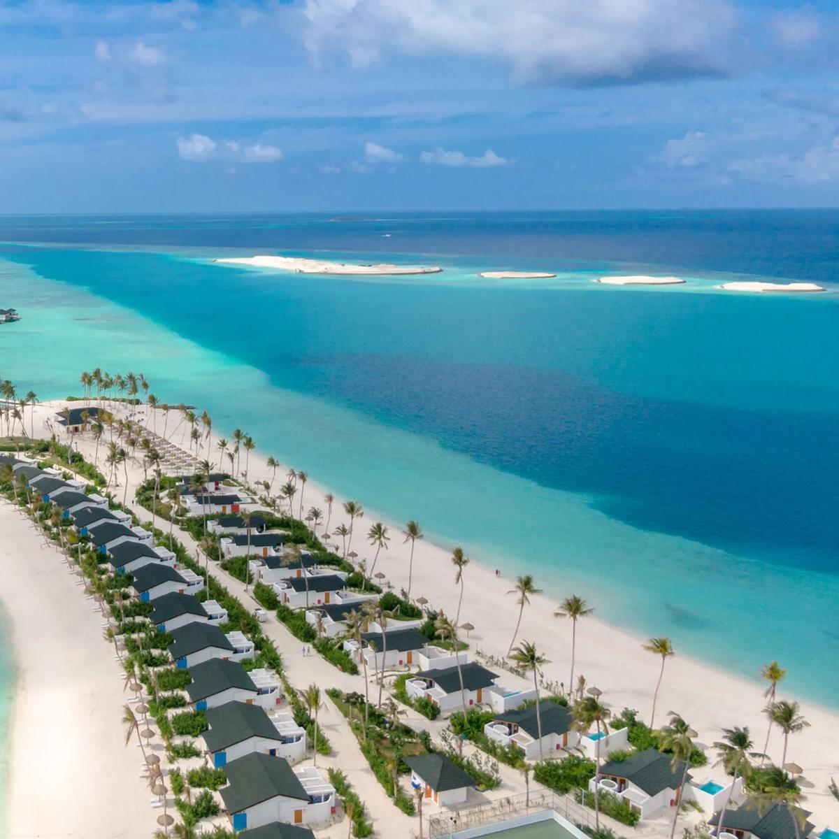 An aerial view of Joy Island's butterfly-shaped outline, overwater villas snaking into the lagoon beside a row of beachfront villas
