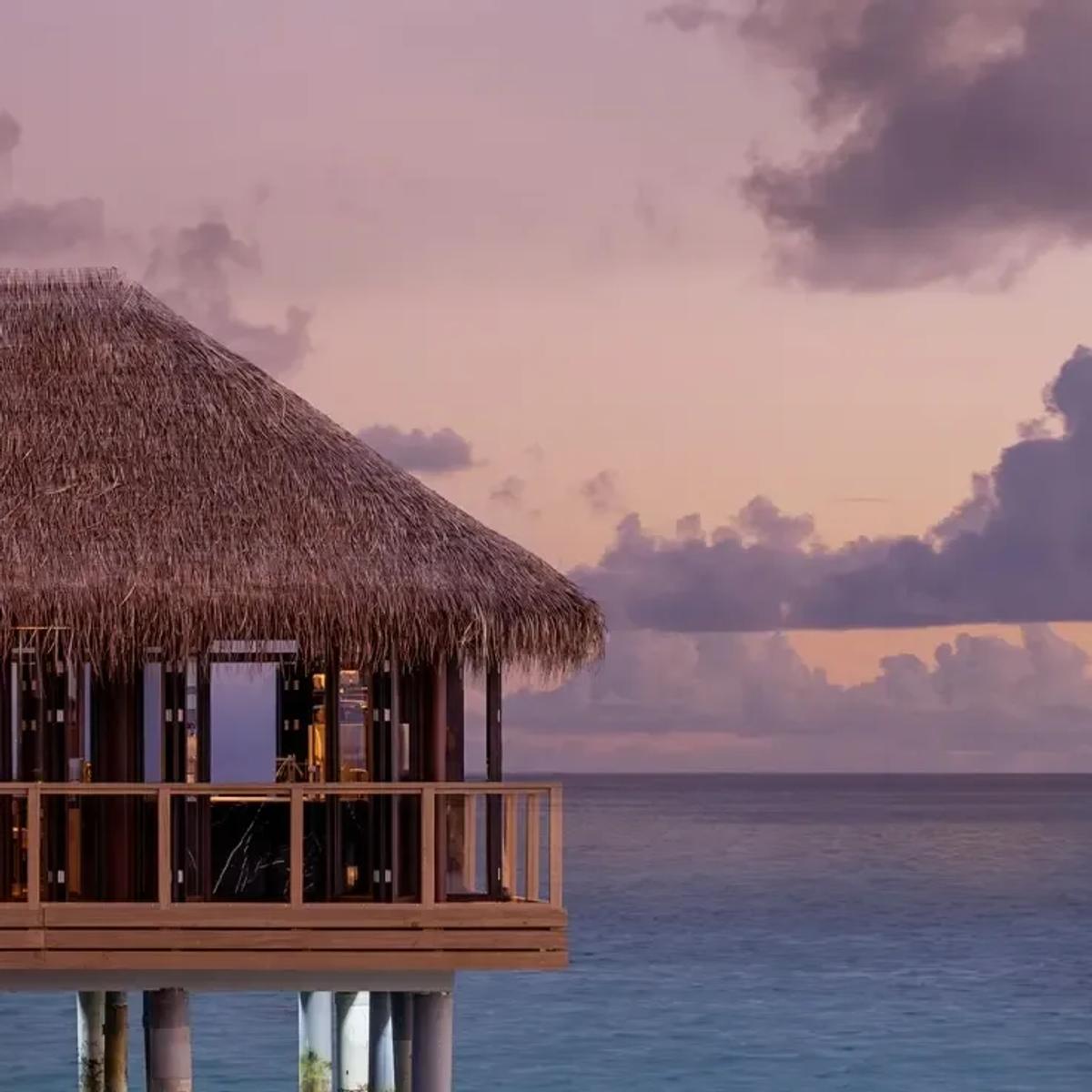 Sora, the overwater restaurant, silhouetted at dusk with its thatched roof over the lagoon