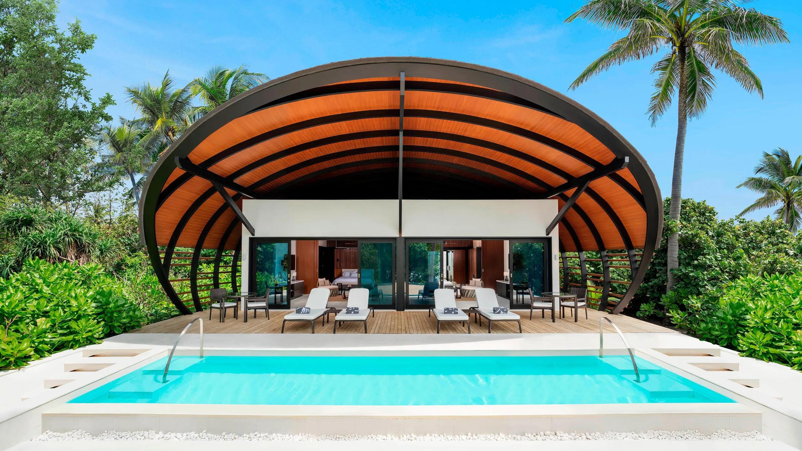 A shell-roofed pool villa set among palms, its private pool running out toward the terrace