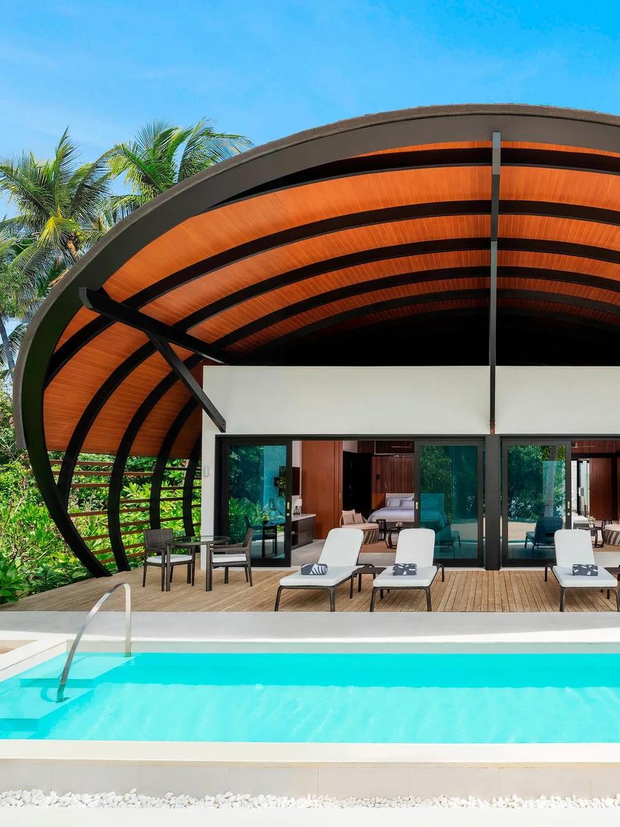 A shell-roofed pool villa set among palms, its private pool running out toward the terrace