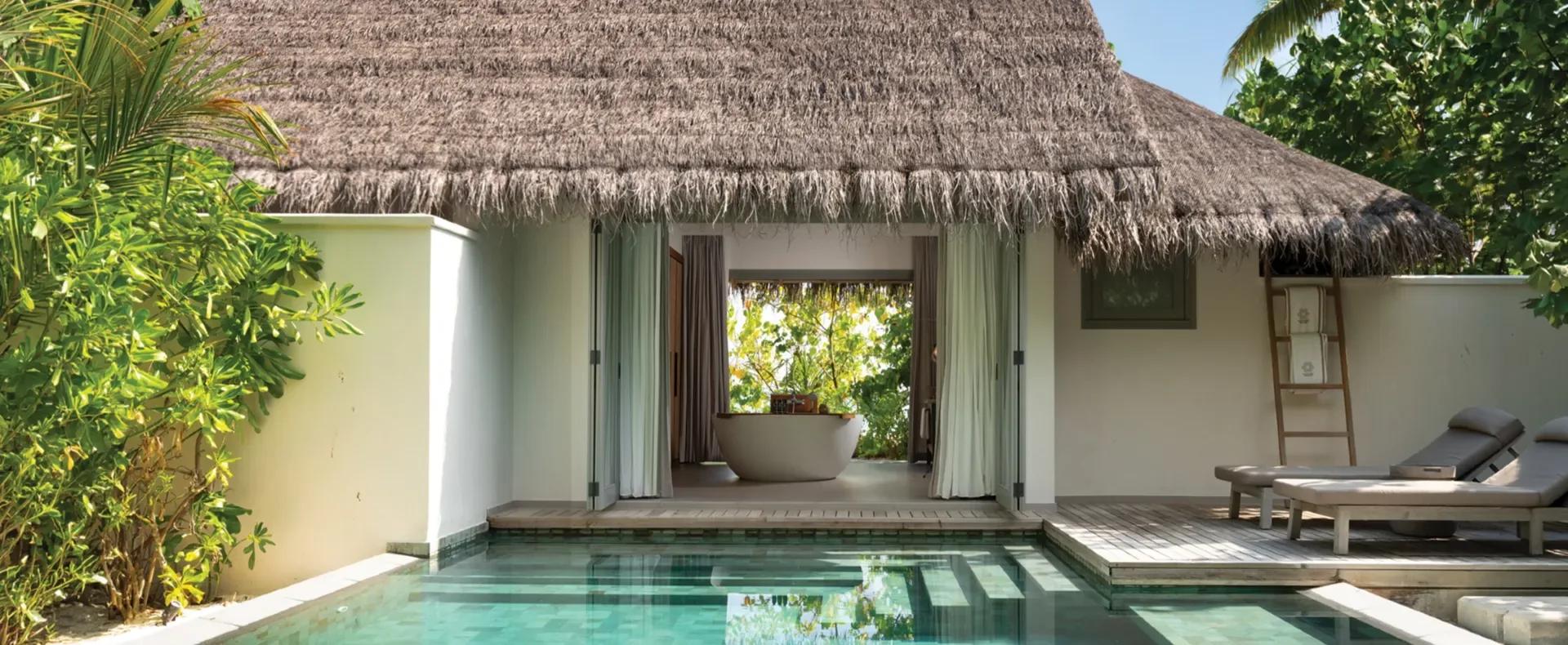 Exterior of a One Bedroom Beach Pool Residence, its thatched roof opening onto a private pool and an outdoor soaking tub