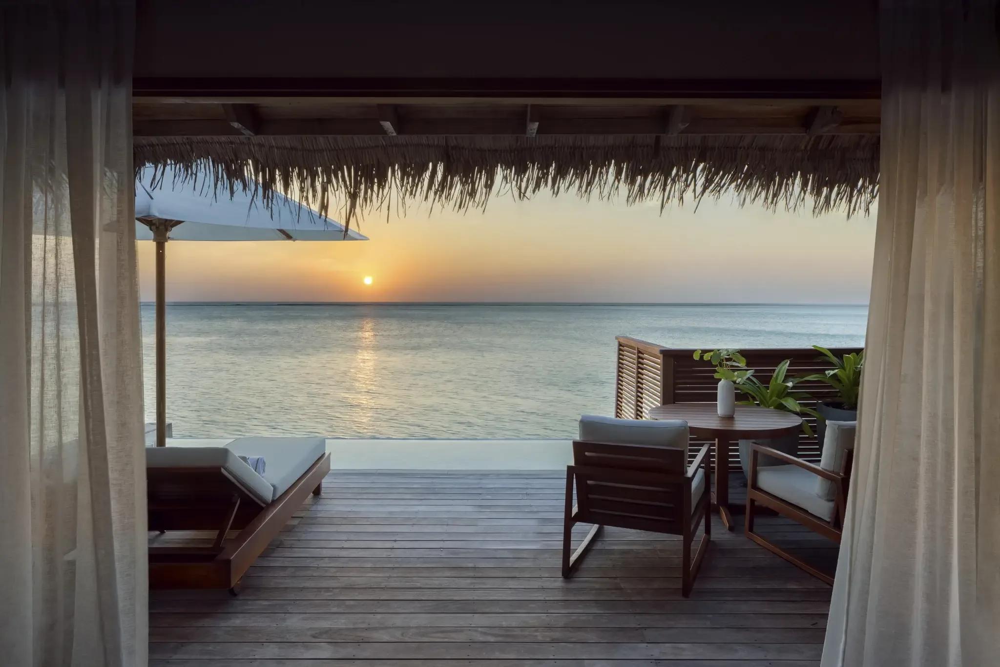 The deck of a Deluxe Water Villa with Pool facing the sunset over open water at Conrad Maldives Rangali