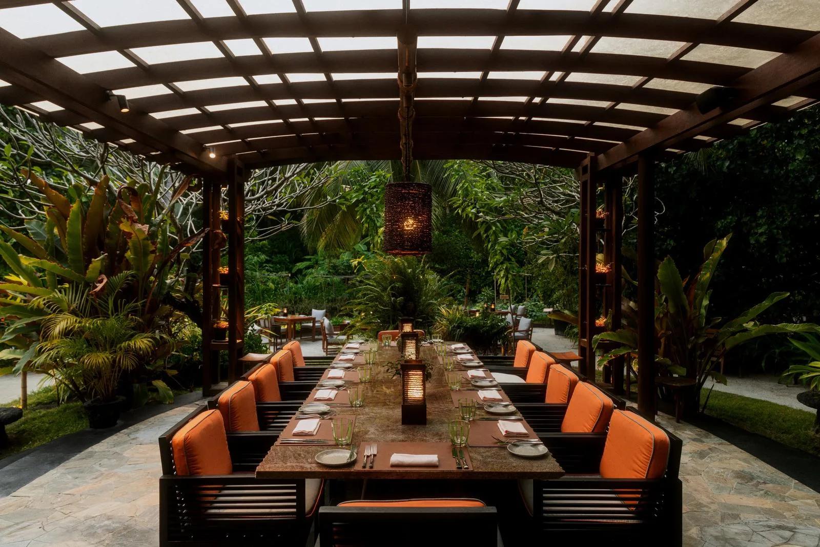 A long communal dining table set beneath a garden pergola at Botanica, One&Only Reethi Rah's farm-to-fork restaurant