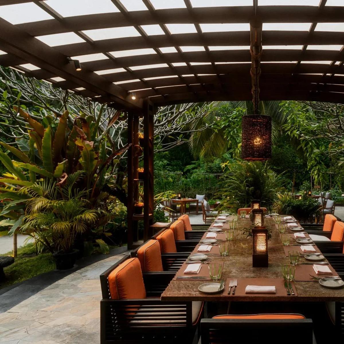 A long communal dining table set beneath a garden pergola at Botanica, One&Only Reethi Rah's farm-to-fork restaurant
